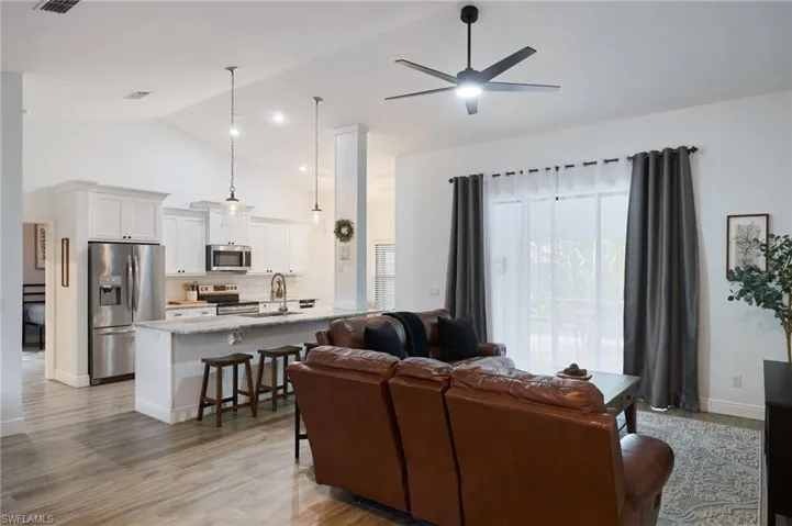 Living room with high vaulted ceiling, sink, light wood-type flooring, and ceiling fan