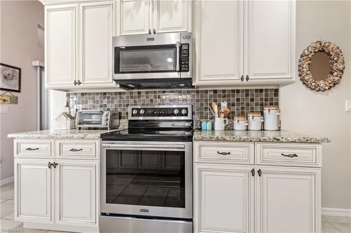 Kitchen featuring light tile patterned floors, appliances with stainless steel finishes, light stone countertops, decorative backsplash, and white cabinets