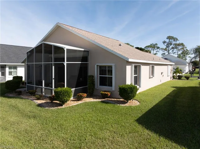 Rear view of house with a lawn, stucco siding, a sunroom, and a shingled roof