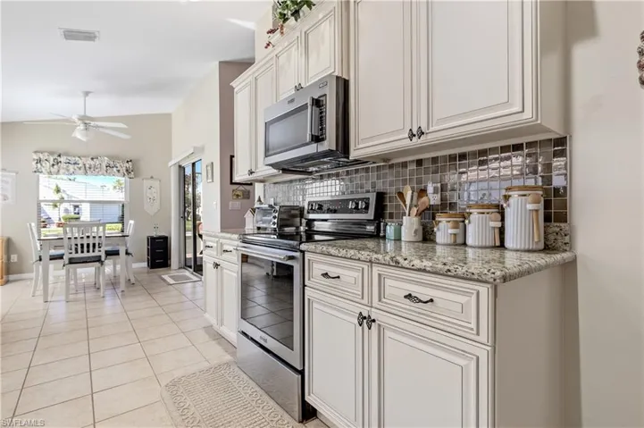 Kitchen with appliances with stainless steel finishes, backsplash, light stone countertops, light tile patterned floors, and ceiling fan