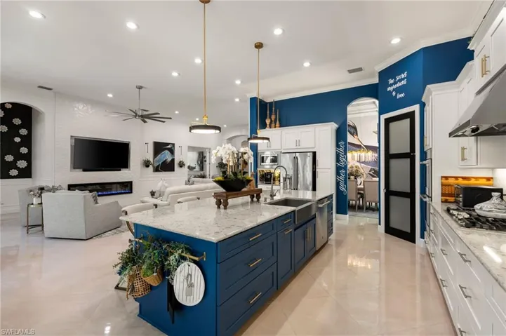 Kitchen featuring arched walkways, white cabinets, open floor plan, ornamental molding, and light stone counters