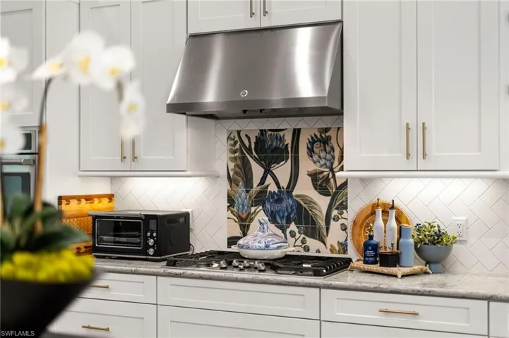 Kitchen featuring white cabinets, under cabinet range hood, tasteful backsplash, and stainless steel appliances