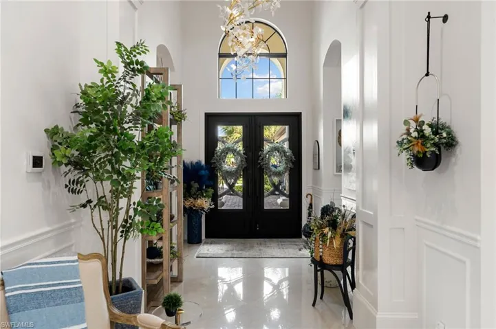 Foyer featuring a decorative wall, a chandelier, a wainscoted wall, arched walkways, and a high ceiling