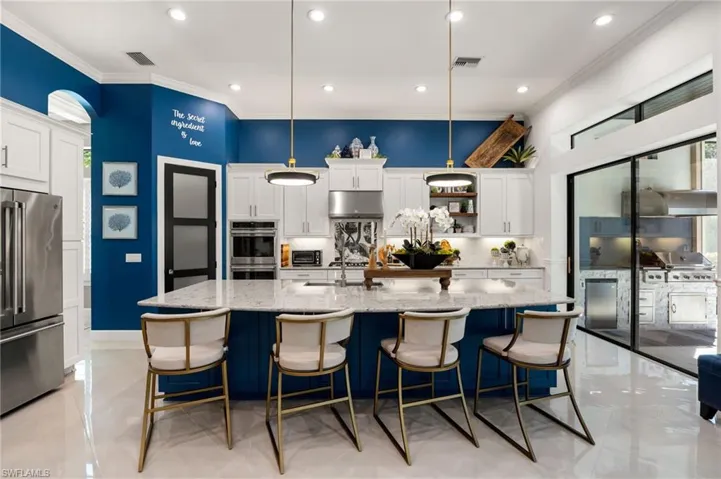 Kitchen with blue cabinets, white cabinetry, stainless steel appliances, pendant lighting, and ornamental molding