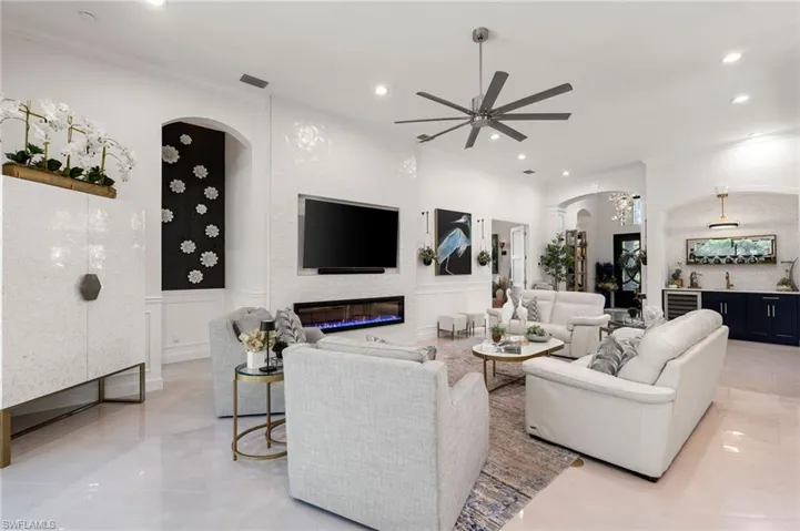 Living room with arched walkways, bar with sink, crown molding, recessed lighting, and a large fireplace