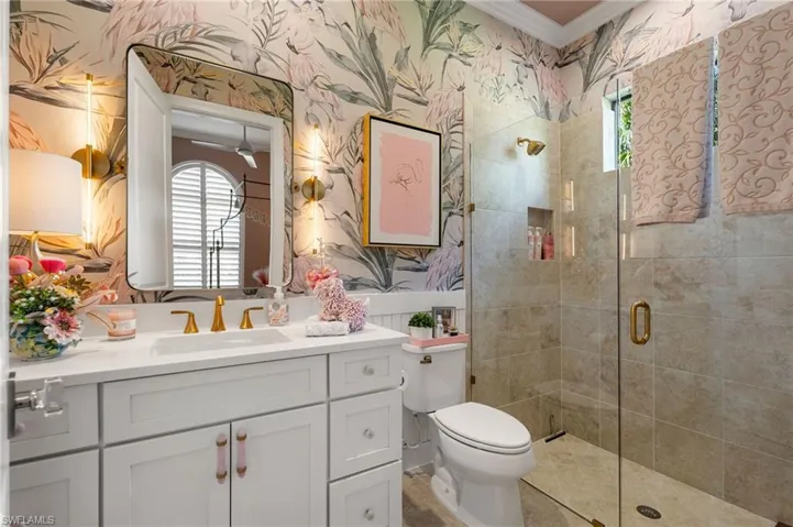 Full bathroom with wallpapered walls, plenty of natural light, a stall shower, vanity, and crown molding