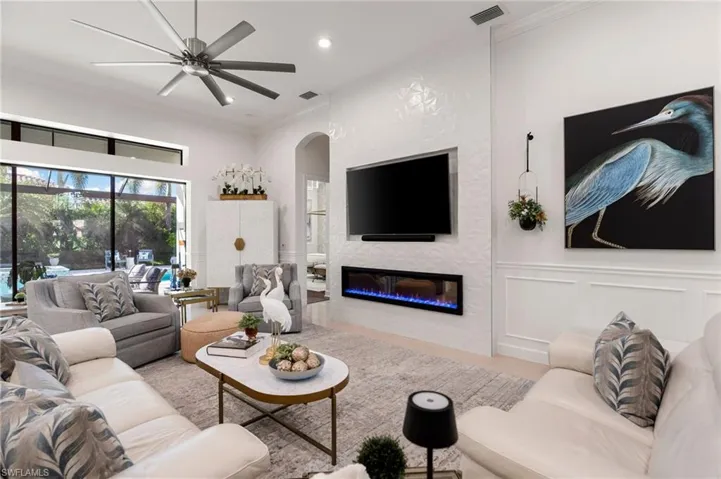 Living room featuring ornamental molding, a large fireplace, a decorative wall, arched walkways, and ceiling fan