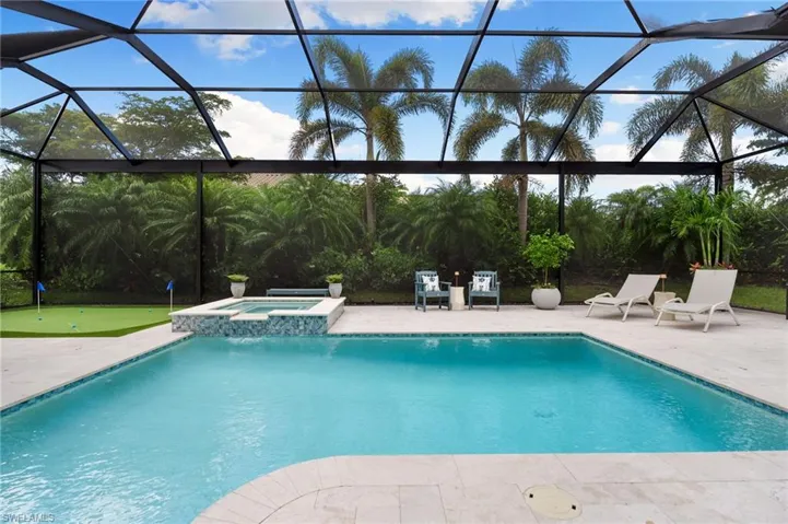 View of swimming pool featuring a sunroom, glass enclosure, a pool with connected hot tub, a patio, and a putting area