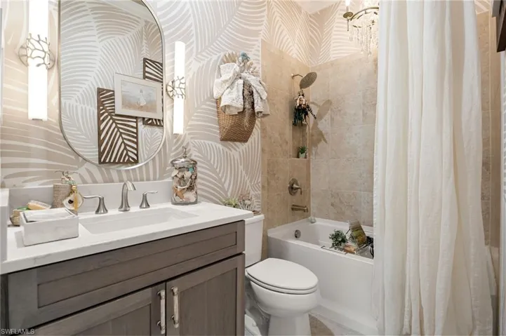 Bathroom featuring wallpapered walls, shower / bath combo with shower curtain, and vanity