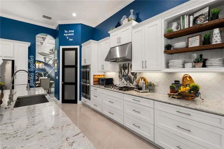 Kitchen featuring light stone counters, white cabinets, crown molding, under cabinet range hood, and open shelves