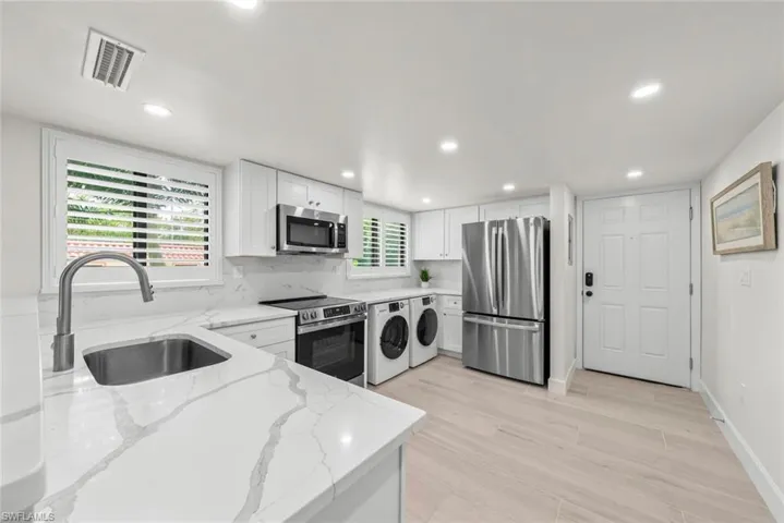 Modern kitchen featuring white shaker cabinetry, stainless steel appliances, white patterned countertops, a stainless steel undermount sink with a gooseneck faucet, and light wood-finish flooring