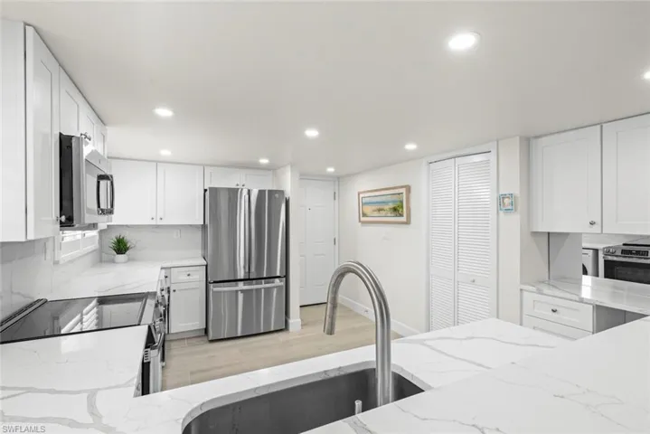 Contemporary kitchen featuring white cabinetry, stainless steel appliances, a tile backsplash, and light-toned wood-finish flooring