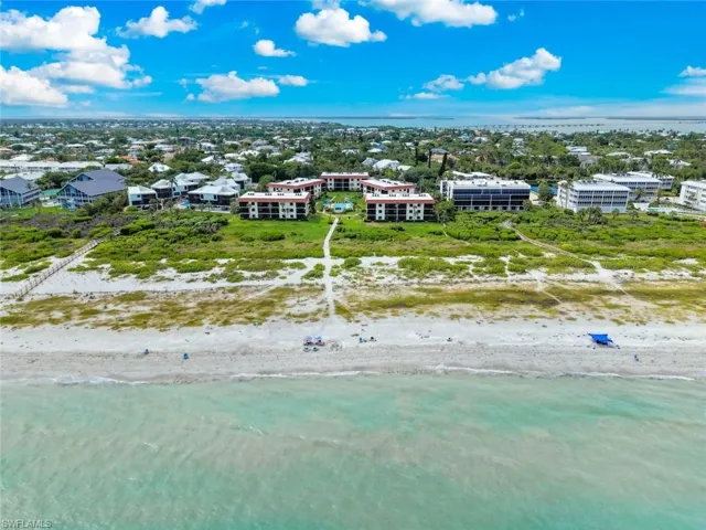 Coastal property featuring direct beach access, multiple residential buildings, and a lush green landscape