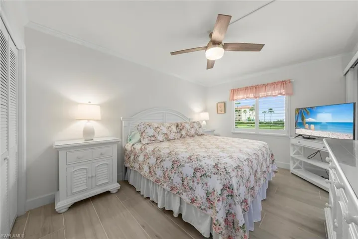 Bedroom featuring wood-finish flooring, a ceiling fan with integrated lighting, a window with plantation shutters, and a louvered bi-fold closet door