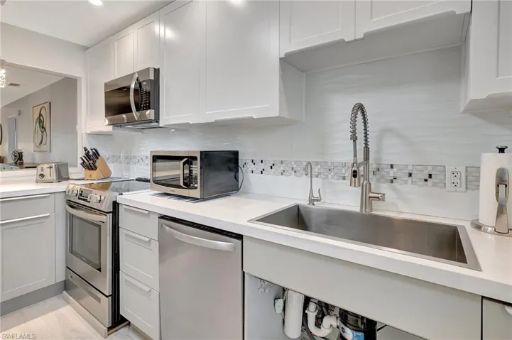 Kitchen featuring appliances with stainless steel finishes, light countertops, tasteful backsplash, and white cabinets