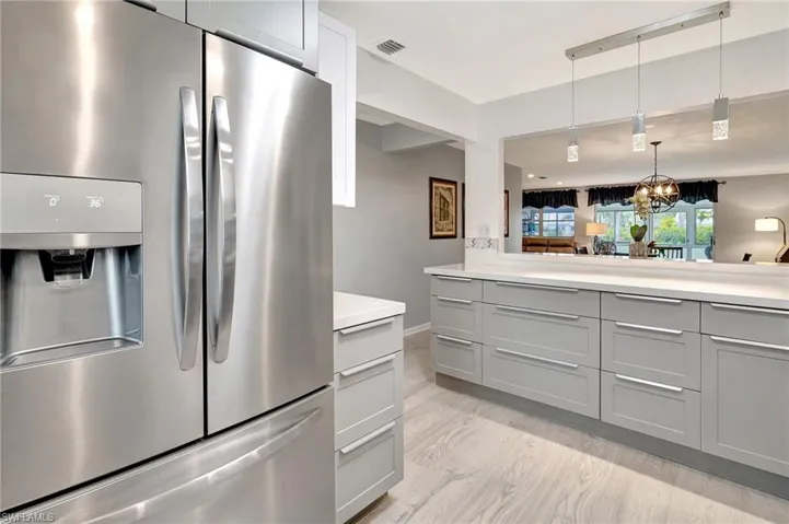 Kitchen with stainless steel fridge, gray cabinetry, light countertops, a chandelier, and pendant lighting
