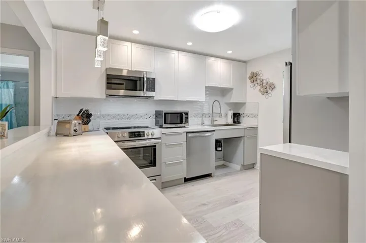 Kitchen with stainless steel appliances, backsplash, light countertops, white cabinetry, and light wood finished floors