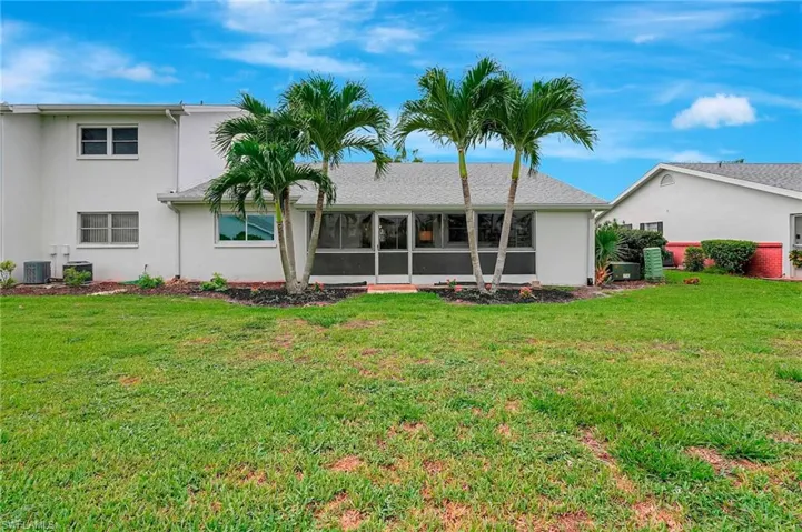 Rear view of house featuring a sunroom, a lawn, and stucco siding