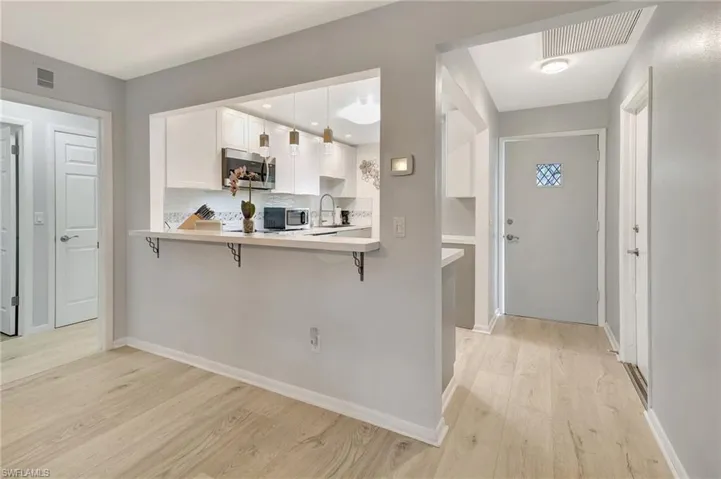 Kitchen with stainless steel microwave, a breakfast bar, light wood-type flooring, and light countertops