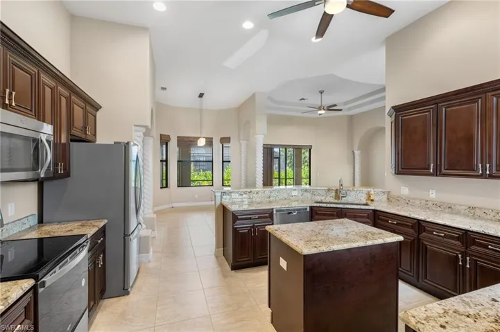 Kitchen featuring appliances with stainless steel finishes, a center island, light stone counters, dark brown cabinetry, and kitchen peninsula