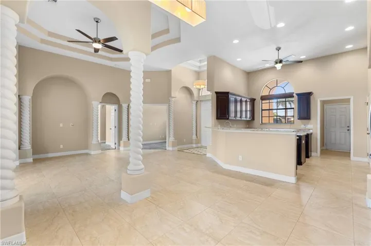 Kitchen featuring decorative columns, a high ceiling, dark brown cabinetry, ceiling fan, and a raised ceiling