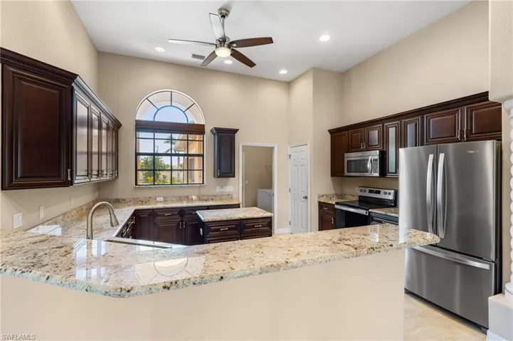 Kitchen featuring sink, light stone counters, dark brown cabinets, kitchen peninsula, and stainless steel appliances