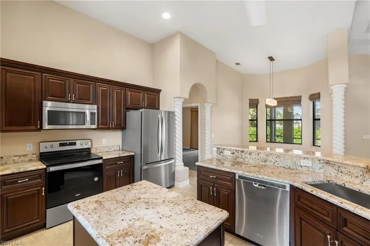 Kitchen with appliances with stainless steel finishes, dark brown cabinets, decorative columns, light stone counters, and decorative light fixtures
