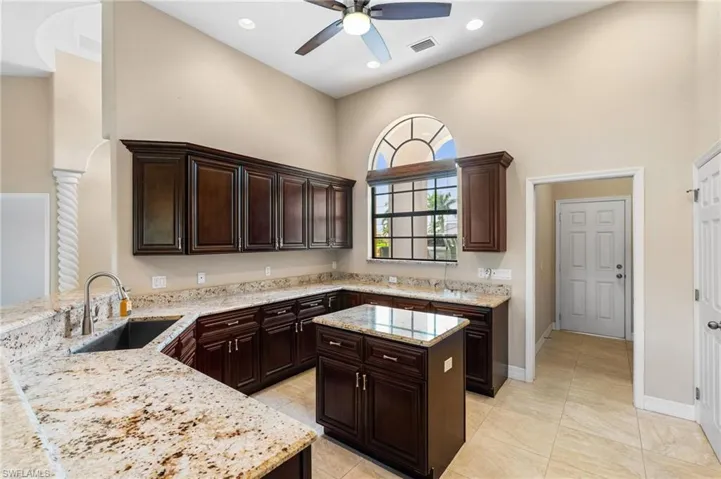 Kitchen featuring sink, ceiling fan, kitchen peninsula, light stone countertops, and dark brown cabinets