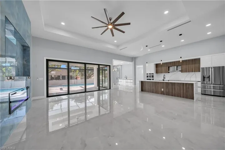 Unfurnished living room with light marble finish flooring, a ceiling fan, a raised ceiling, recessed lighting, and a towering ceiling