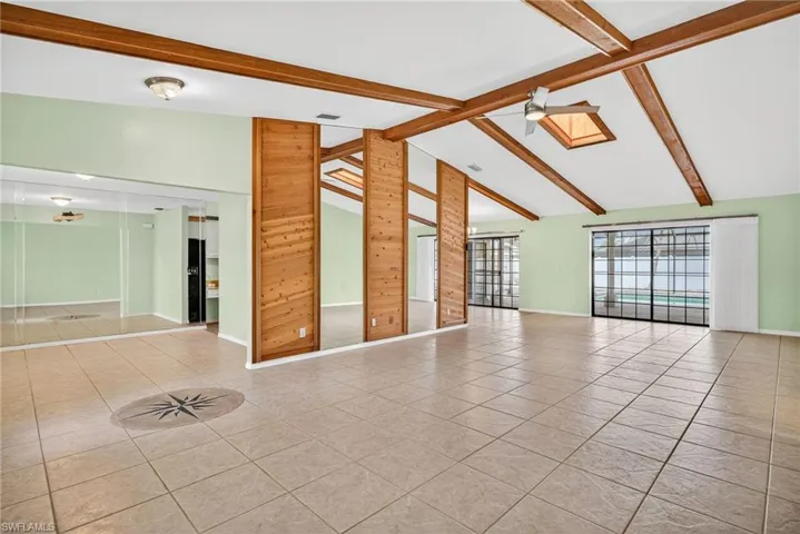Unfurnished room with beam ceiling, tile patterned flooring, wooden walls, a ceiling fan, and high vaulted ceiling