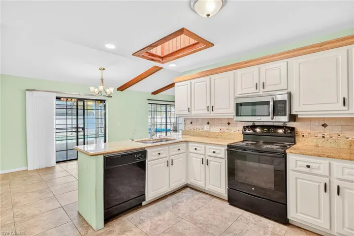 Kitchen featuring black appliances, decorative backsplash, a skylight, white cabinetry, and recessed lighting