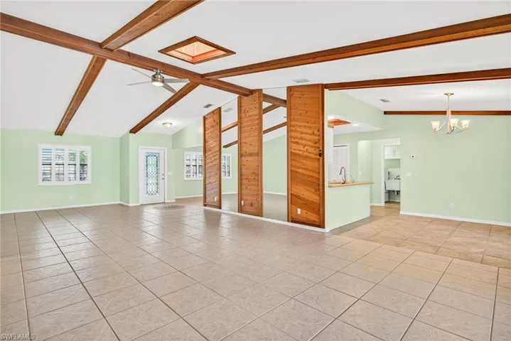 Unfurnished living room featuring light tile patterned floors, beamed ceiling, a chandelier, a ceiling fan, and high vaulted ceiling