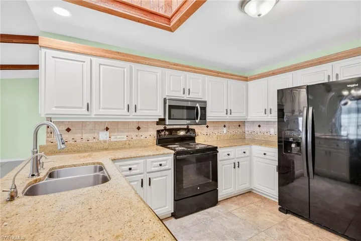 Kitchen with black appliances, tasteful backsplash, light stone countertops, and white cabinetry