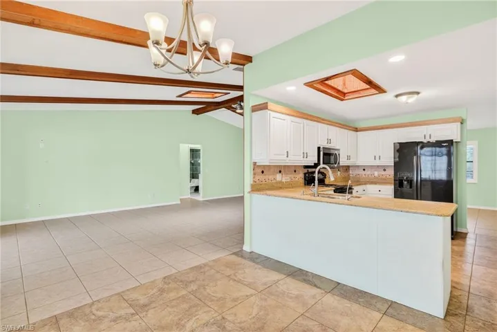 Kitchen featuring decorative light fixtures, tasteful backsplash, light stone countertops, black refrigerator with ice dispenser, and white cabinets