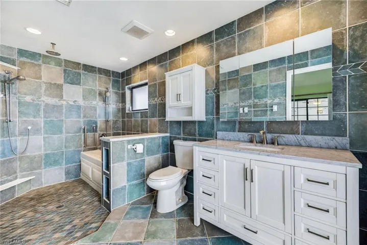 Bathroom featuring tile walls, recessed lighting, dark tile patterned flooring, vanity, and a stall shower