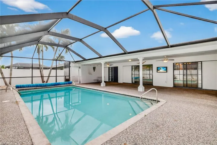 View of pool with glass enclosure, ceiling fan, a sunroom, and a patio area