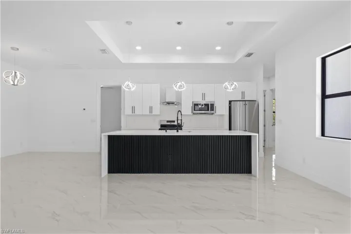 Kitchen featuring a raised ceiling, marble finish floor, appliances with stainless steel finishes, and wall chimney exhaust hood