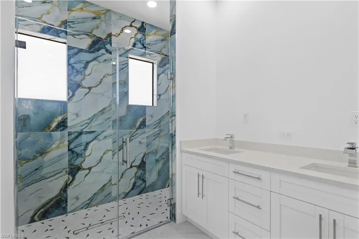 Bathroom with double vanity, a marble finish shower, a sink, and marble finish floor