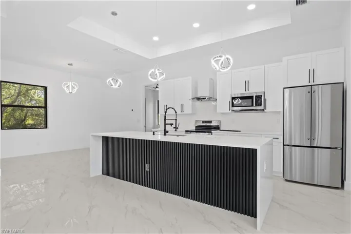 Kitchen featuring wall chimney range hood, a sink, stainless steel appliances, white cabinetry, and a tray ceiling