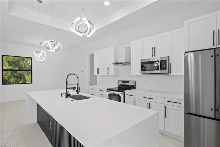 Kitchen with appliances with stainless steel finishes, a sink, white cabinets, a notable chandelier, and wall chimney exhaust hood