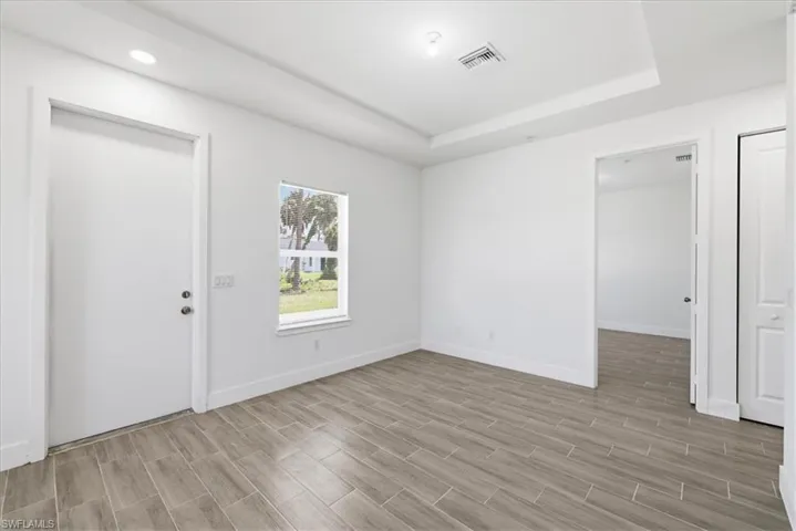 Spacious room featuring wood-finish tile flooring, a window offering exterior views, a tray ceiling, and recessed lighting