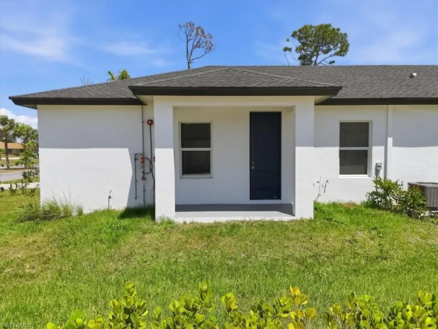 White stucco exterior featuring a covered entry, dark paneled door, and dark asphalt shingle roof