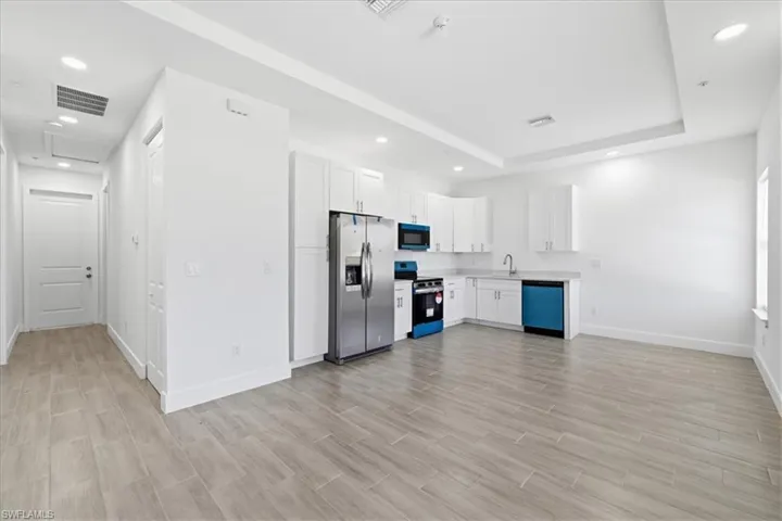 Open-concept living area featuring a kitchen with stainless steel appliances, white cabinetry, and light countertops