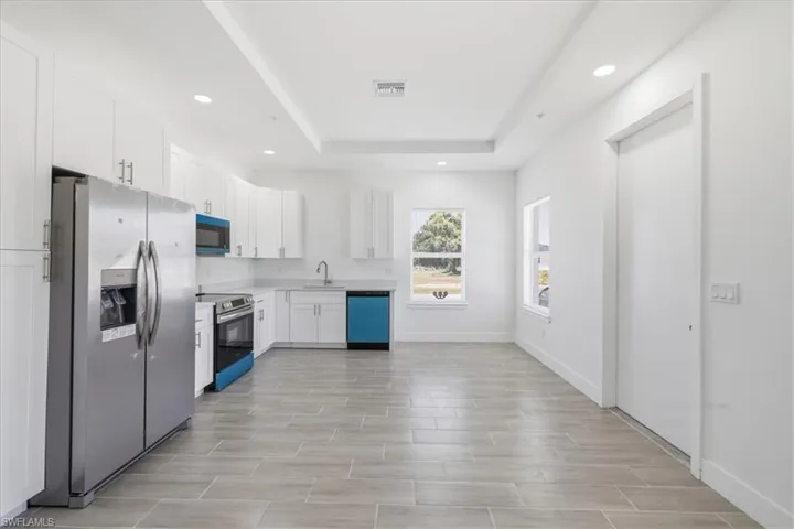Kitchen featuring stainless steel appliances, white cabinetry, a light-toned countertop, a window with outdoor scenery, and wood-finish flooring