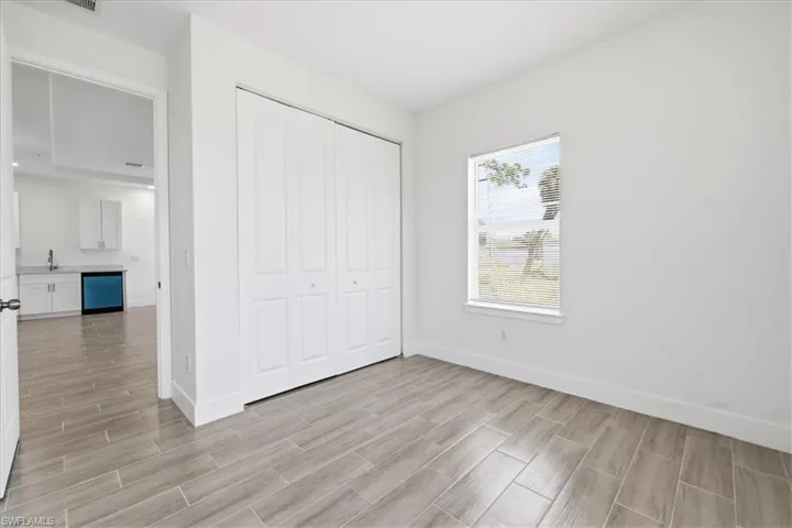 Bedroom featuring wood-finish tile flooring, white bi-fold closet doors, a single window, and white painted walls