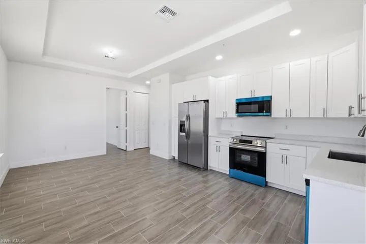 Spacious open-concept kitchen and living area featuring white cabinetry, stainless steel appliances, light-toned countertops, and wood-finish tile flooring