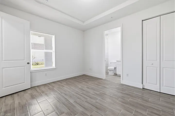 Room featuring wood-finish flooring, a tray ceiling, and white baseboards