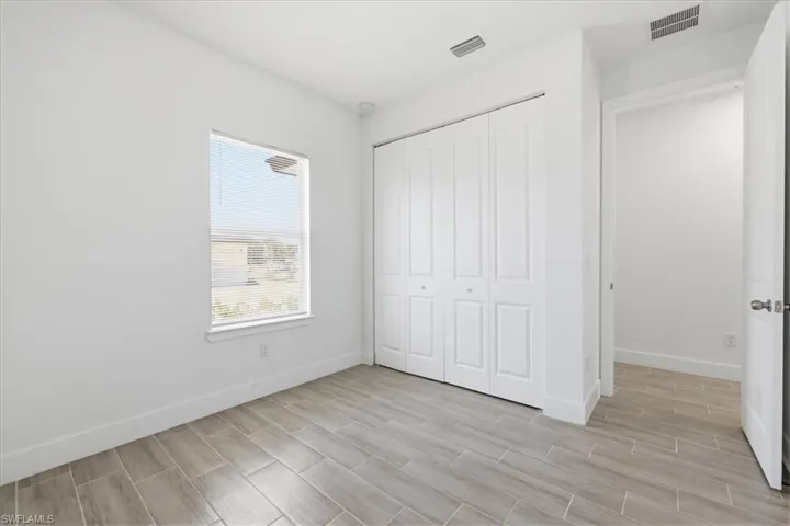 Interior room featuring white walls, wood-finish tile flooring, and a window with horizontal blinds