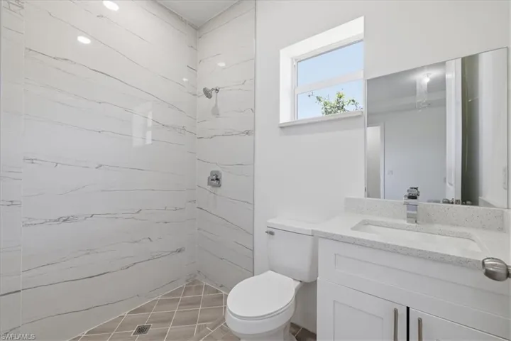 Modern bathroom featuring a walk-in shower with white marble-look tile walls, a built-in vanity with a light-colored speckled countertop, an integrated sink, and a large wall-mounted mirror