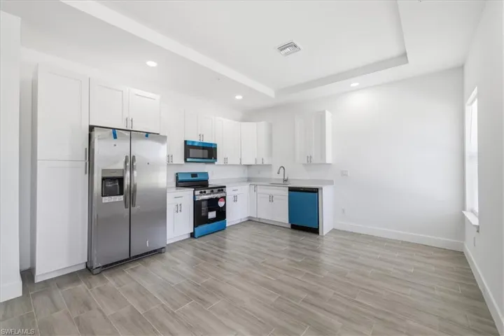 Kitchen featuring white shaker cabinetry, stainless steel appliances, light-toned countertops, wood-finish tile flooring, and recessed lighting